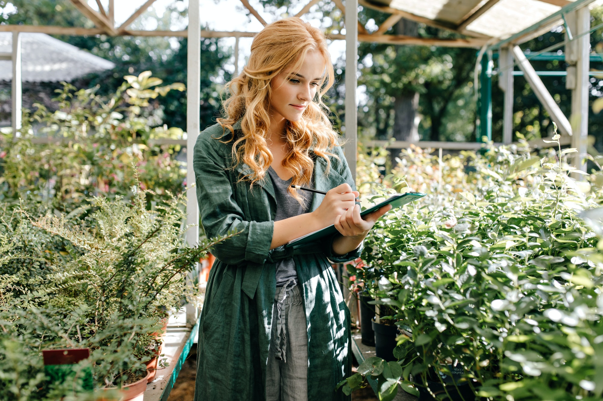 curly-girl-botanist-exploring-plants-in-greenhouse-woman-in-khaki-tunic-makes-notes-in-tablet-.jpg